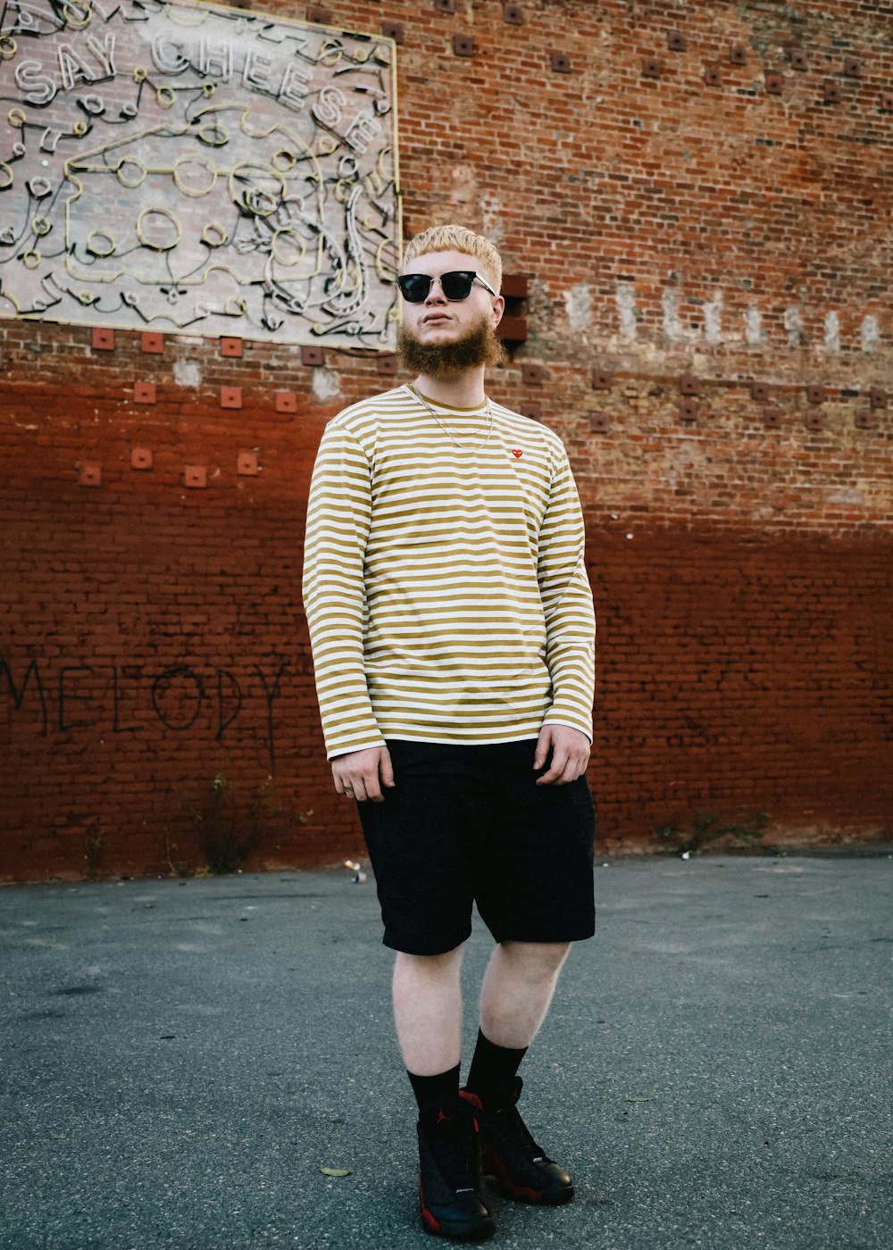 man in green sweater and black shorts standing beside brown brick wall