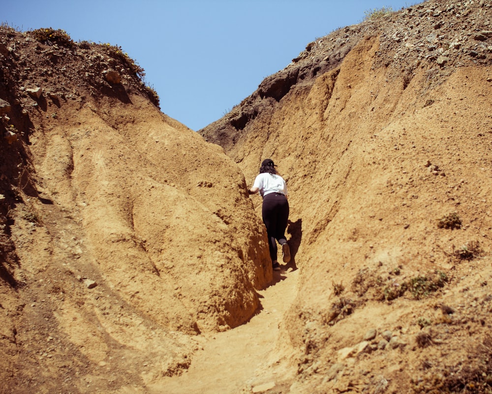 man in white t-shirt and black shorts walking on brown rocky hill during daytime