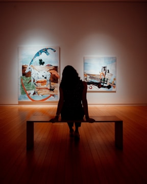 woman in black dress standing on brown wooden floor looking at artwork