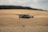 A drone is flying over an expansive, golden field, likely a wheat field, with gentle rolling hills in the background. The sky appears cloudy, with soft lighting casting a serene glow over the landscape.