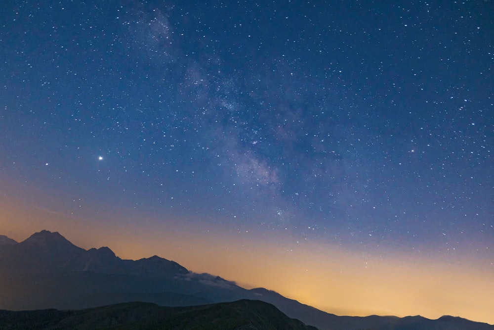 silhouette of mountains under blue sky with stars during night time