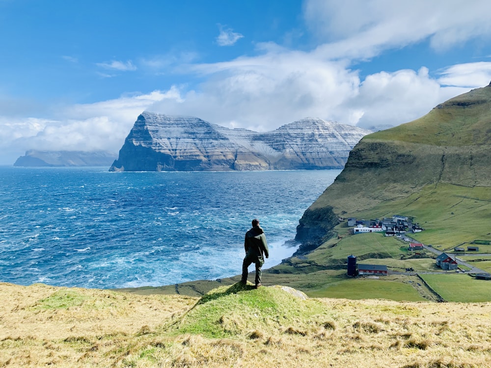 man in black jacket standing on green grass field near body of water during daytime