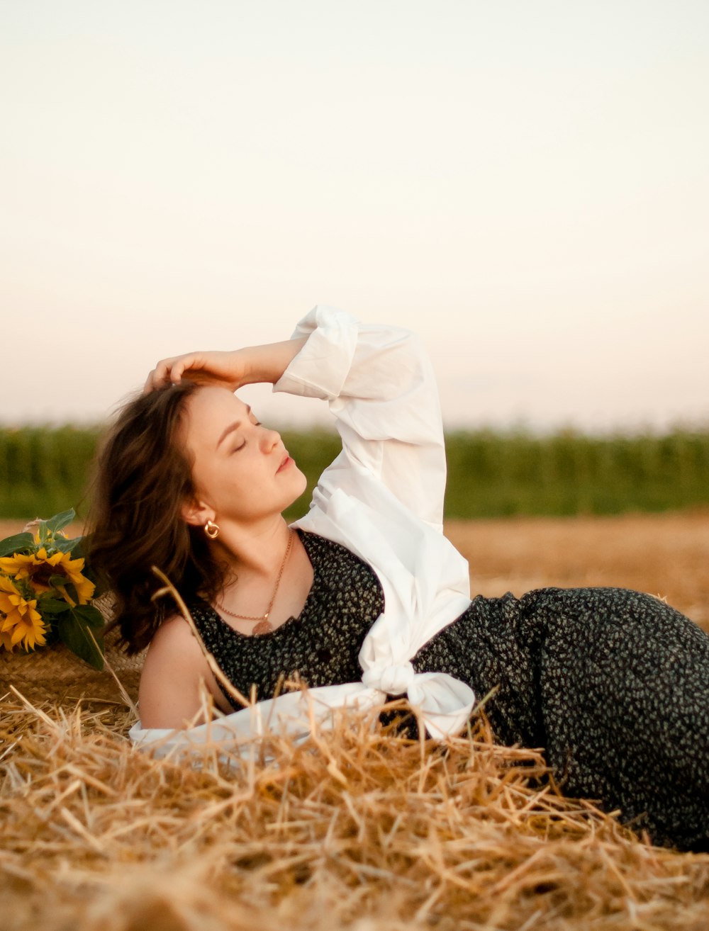 woman in black and white floral dress lying on brown grass field during daytime