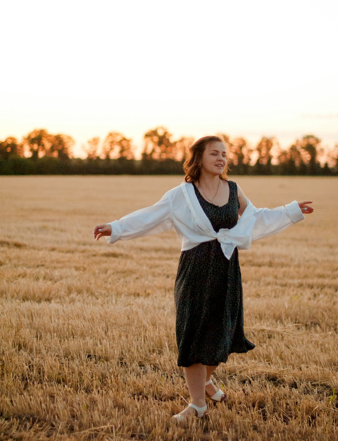woman in white long sleeve shirt and black skirt standing on brown grass field during sunset
