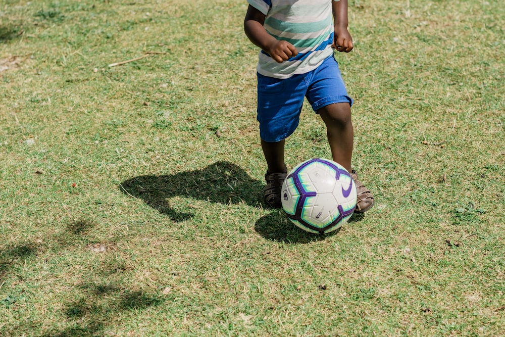 man in white t-shirt and blue shorts playing soccer during daytime