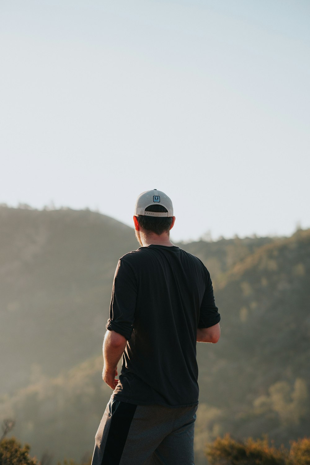 man in black crew neck t-shirt and white cap standing on mountain during daytime