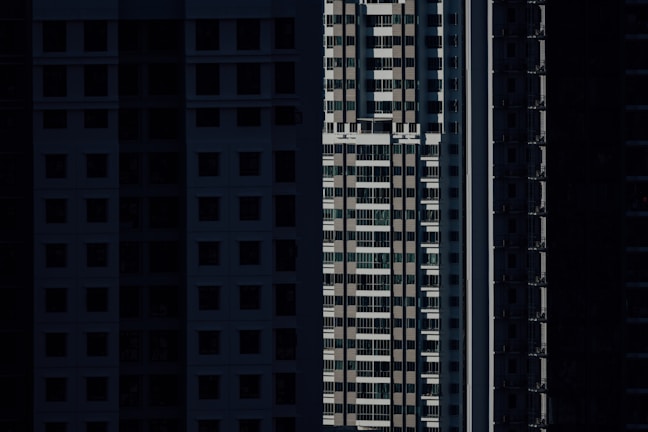 High-rise residential buildings are depicted with shadow-covered facades, highlighting vertical lines and geometric patterns in an urban setting.