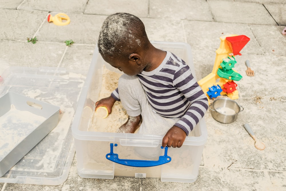 baby in white and black stripe long sleeve shirt sitting on blue and white plastic container