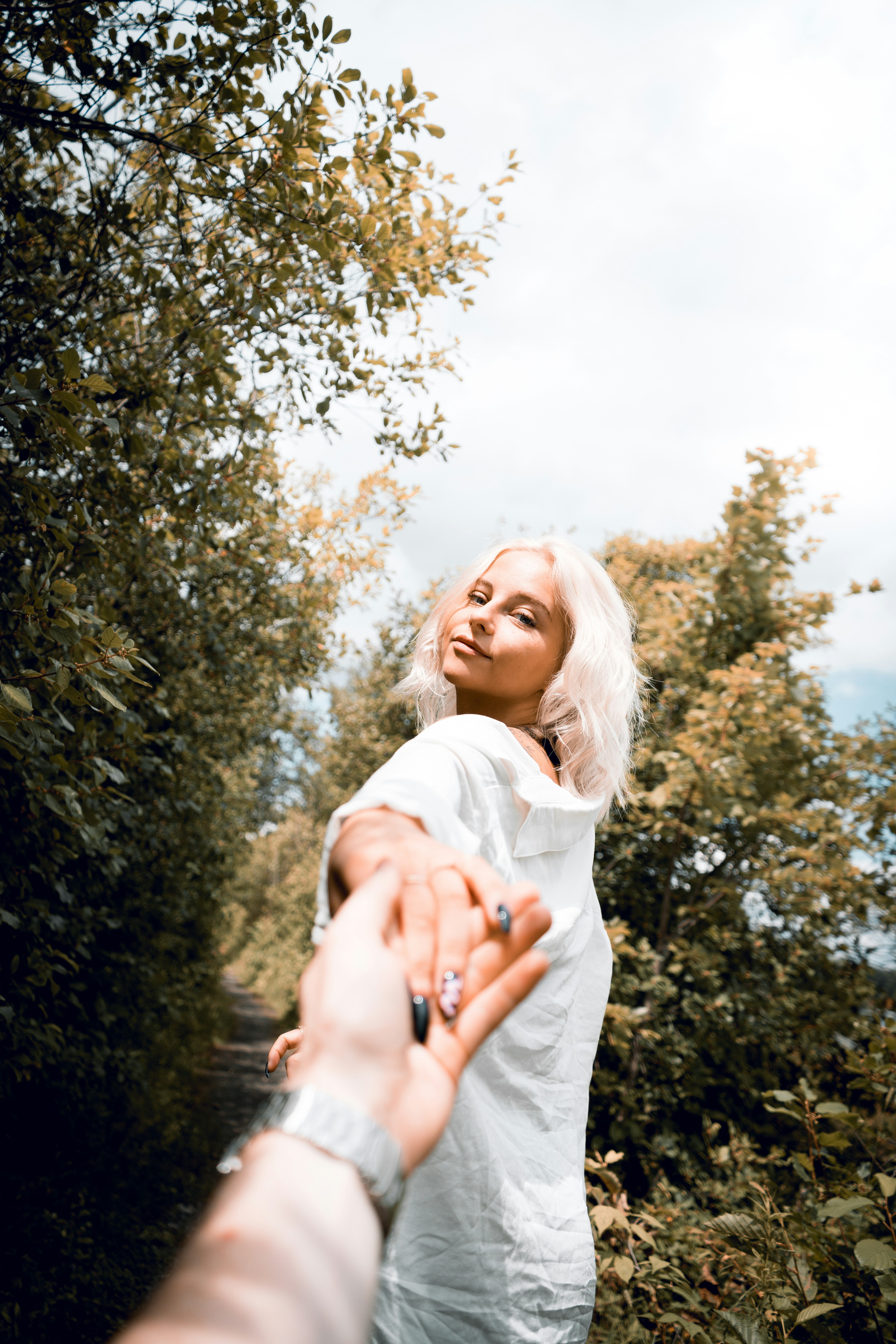 Woman in white long sleeve shirt standing near green tree during ...