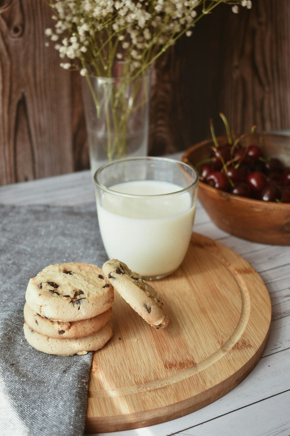 茶色の木製のまな板にクッキーの横にミルクが入った透明なコップ