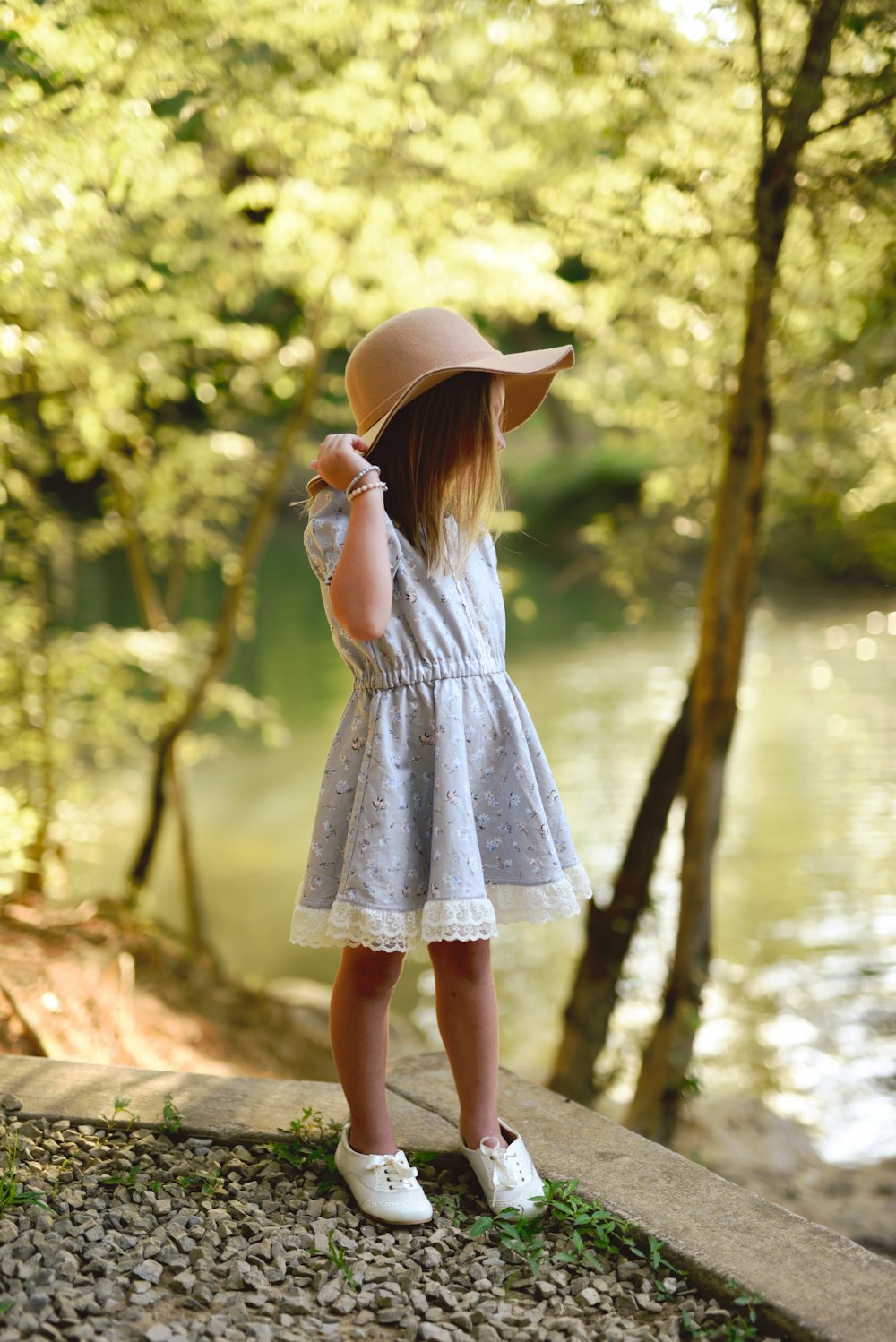 Frau in grauem Kleid mit braunem Sonnenhut, die tagsüber in der Nähe des Gewässers steht