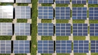Rows of solar panels arranged in a grid-like pattern, set on a field of green grass. The panels are aligned in a north-south direction, suggesting they are positioned for optimal sunlight exposure.