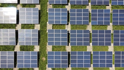 Rows of solar panels arranged in a grid-like pattern, set on a field of green grass. The panels are aligned in a north-south direction, suggesting they are positioned for optimal sunlight exposure.