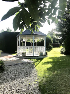 White gazebo tent set up in a sunny garden for a small outdoor gathering.