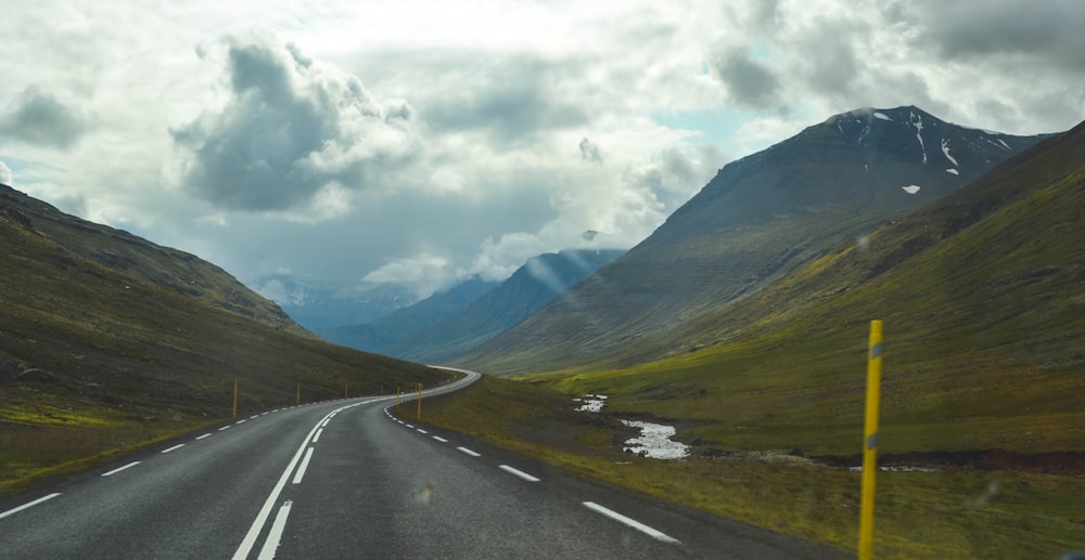 gray asphalt road near green mountains under white clouds during daytime