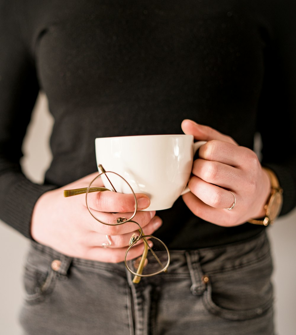 person in black long sleeve shirt holding white ceramic mug