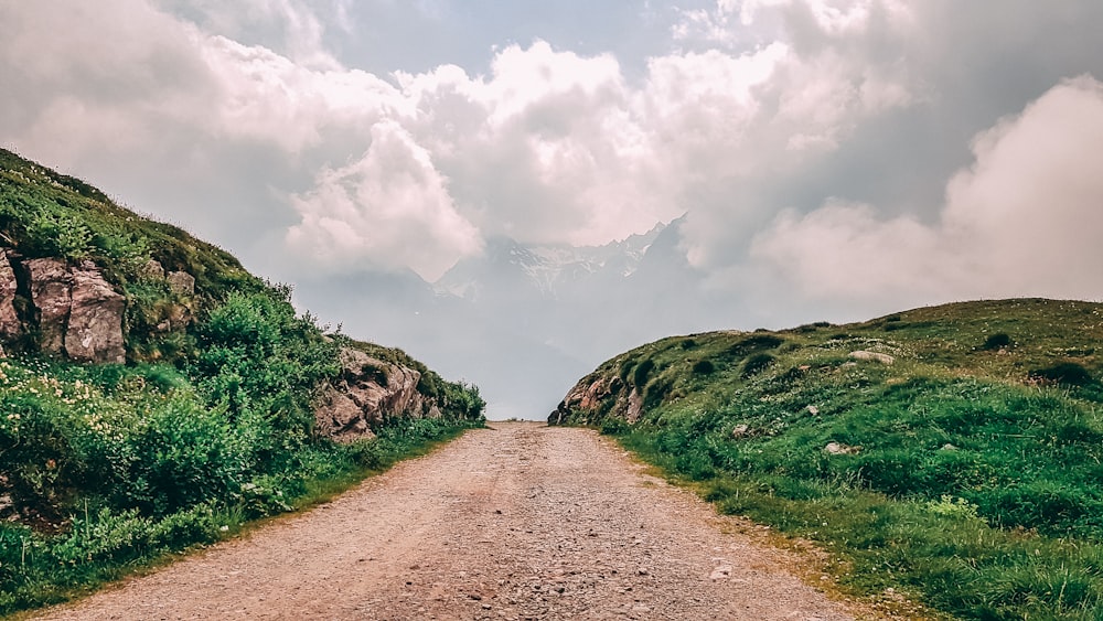 brown dirt road between green grass field under white clouds