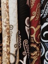 Upright bolts of textile featuring intricate patterns and designs. These textiles showcase various traditional motifs with swirling and ornate details in different colors and textures.