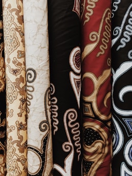 Upright bolts of textile featuring intricate patterns and designs. These textiles showcase various traditional motifs with swirling and ornate details in different colors and textures.