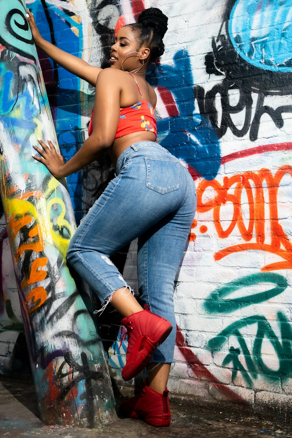 woman in blue denim jeans and red sports bra leaning on wall with graffiti