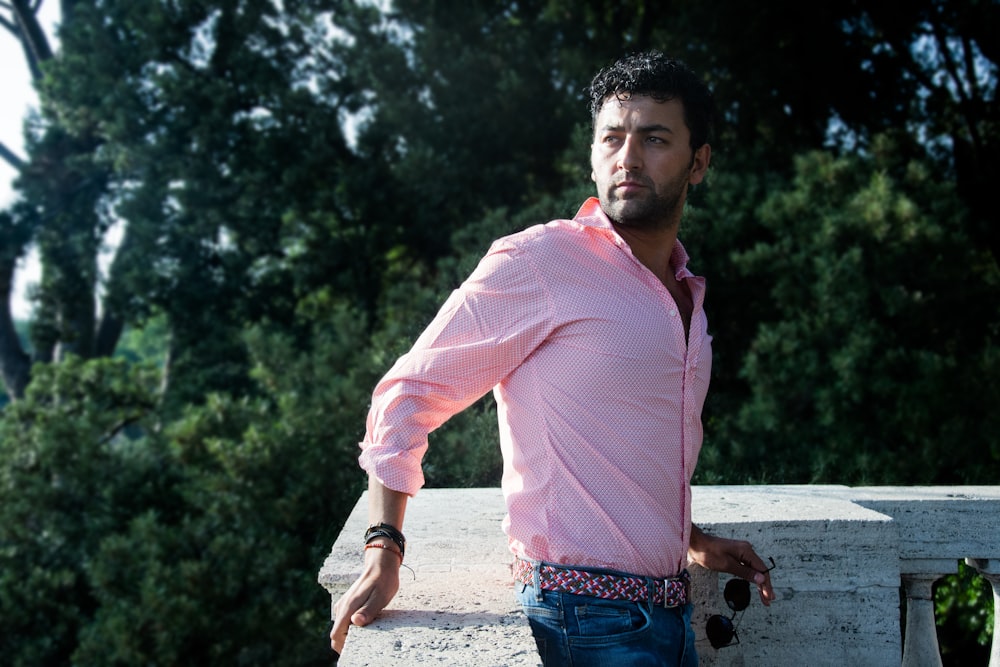 man in pink dress shirt and blue denim jeans standing on road during daytime