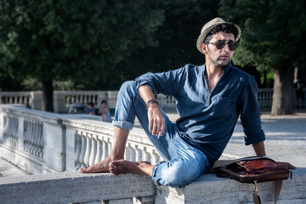 man in blue dress shirt and blue denim jeans sitting on concrete bench during daytime