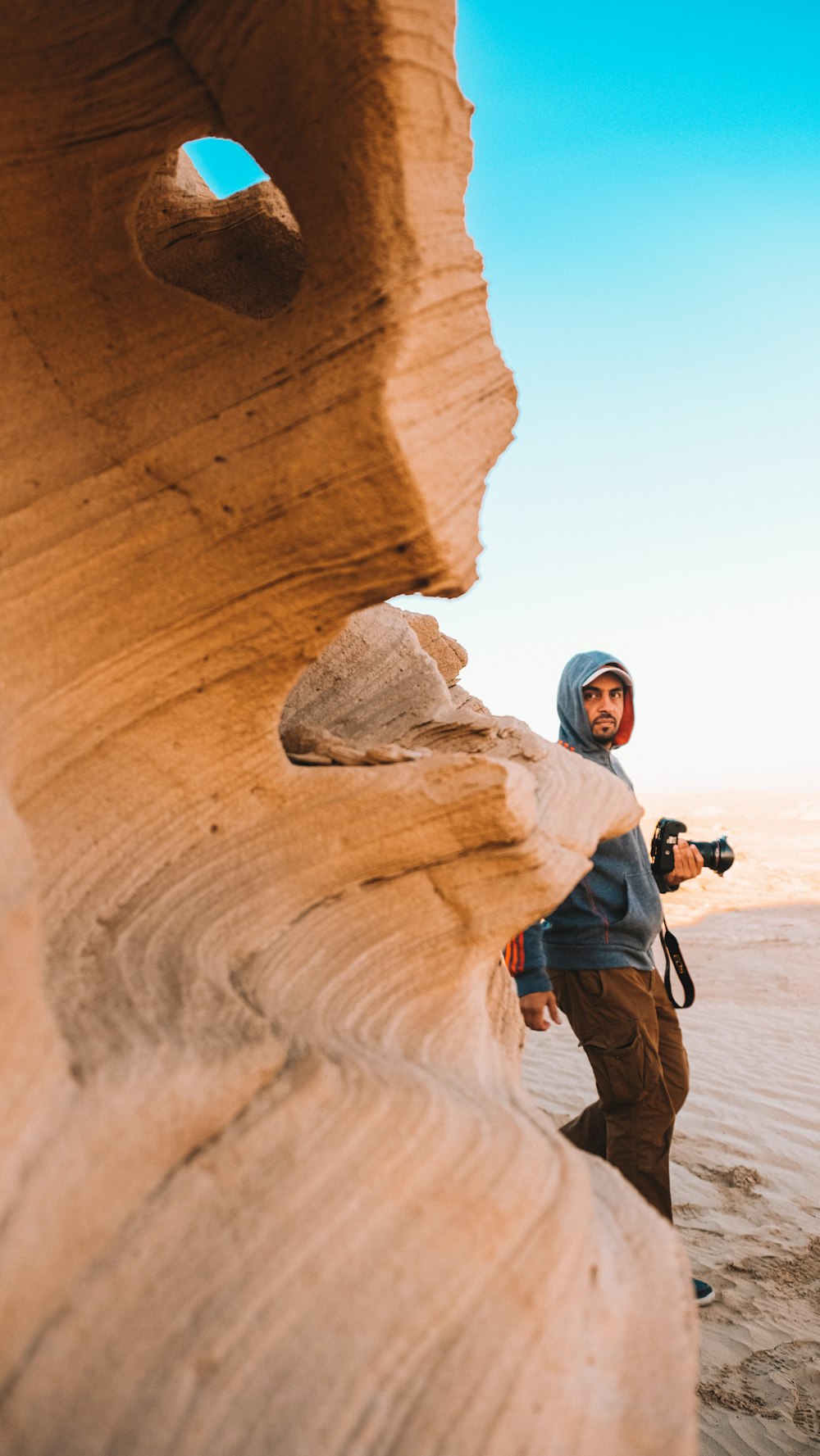 man in blue jacket and black pants standing on brown rock formation during daytime