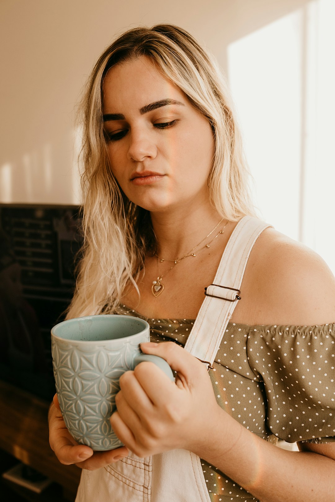 woman in white tank top holding white and green ceramic mug