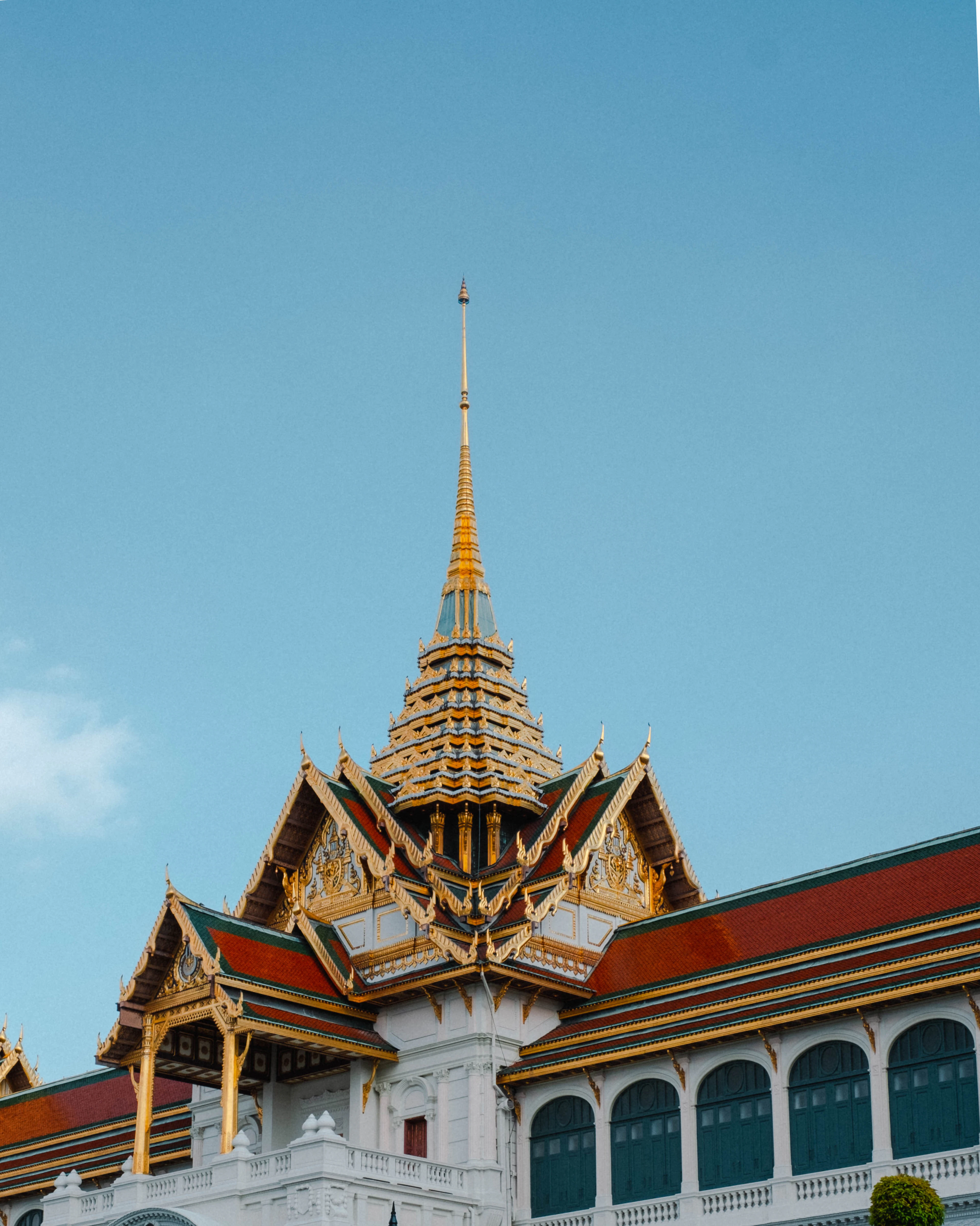 A gilded Thai prang rising against a clear blue sky, its tiers stepping to a fine point