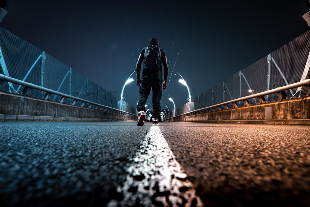 Mann in schwarzer Jacke und schwarzer Hose fährt nachts Fahrrad auf der Brücke