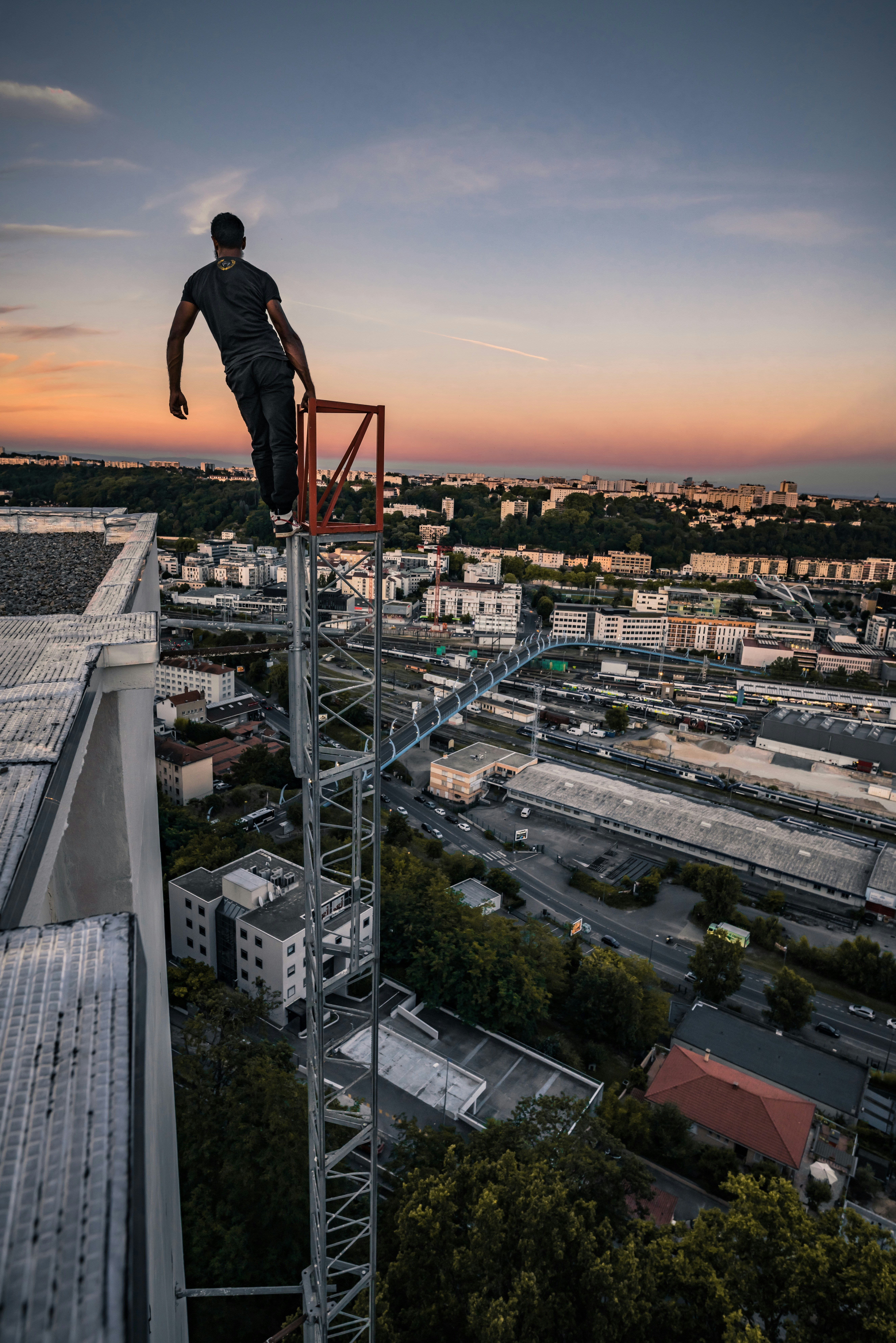 homme en veste noire et pantalon debout sur le toit du bâtiment pendant le coucher du soleil