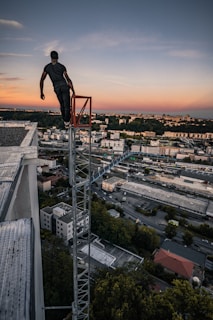 man in black jacket and pants standing on top of building during sunset