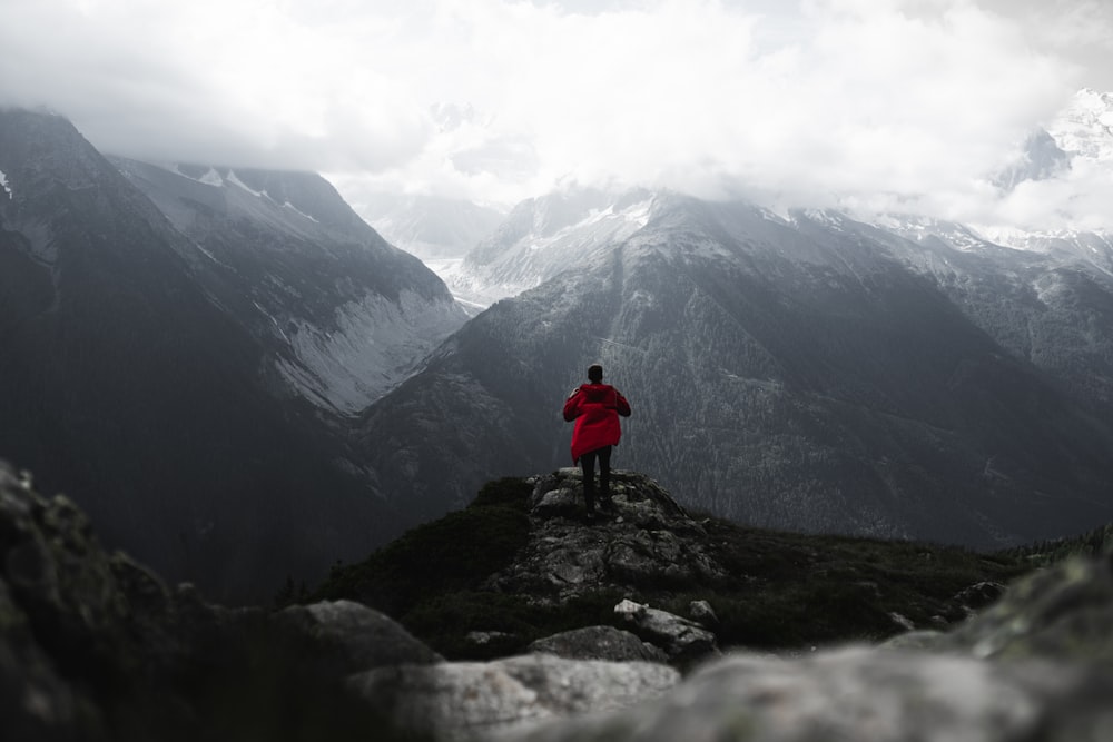 Persona in giacca rossa in piedi sulla montagna rocciosa durante il giorno