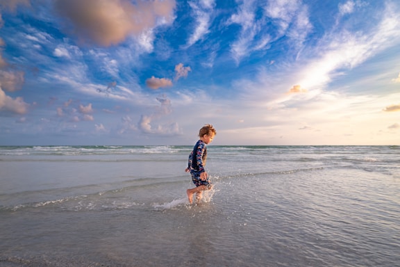 girl in black and white plaid dress shirt and black shorts running on siesta beach during daytime
