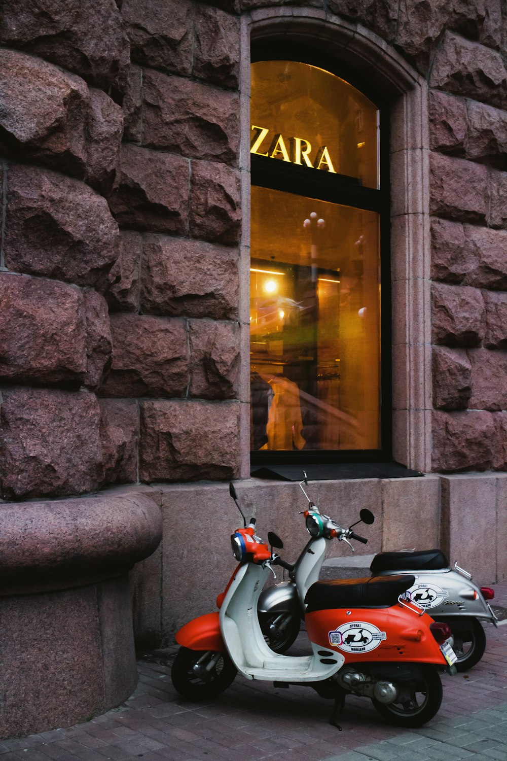 red and black motor scooter parked beside brown brick wall