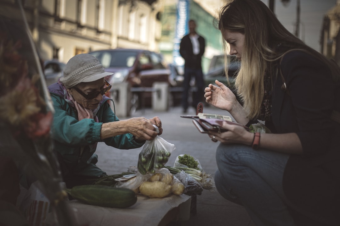 woman in blue denim jacket holding white smartphone, Street market of farm products.