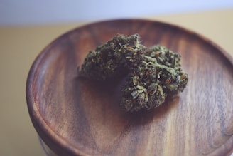 Two cannabis buds rest on a simple wooden dish, with the focus on the texture of the buds and the wood grain. The lighting is soft, creating a calm atmosphere.