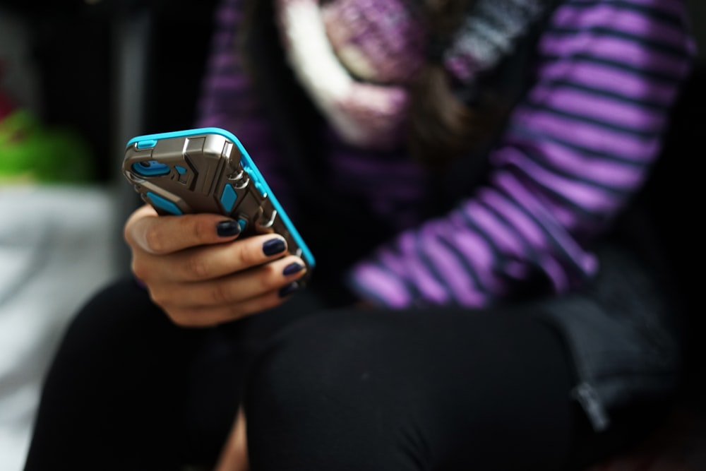 woman in purple and black stripe long sleeve shirt holding blue smartphone