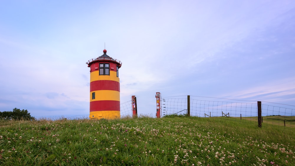 red and brown lighthouse on green grass field under white clouds during daytime