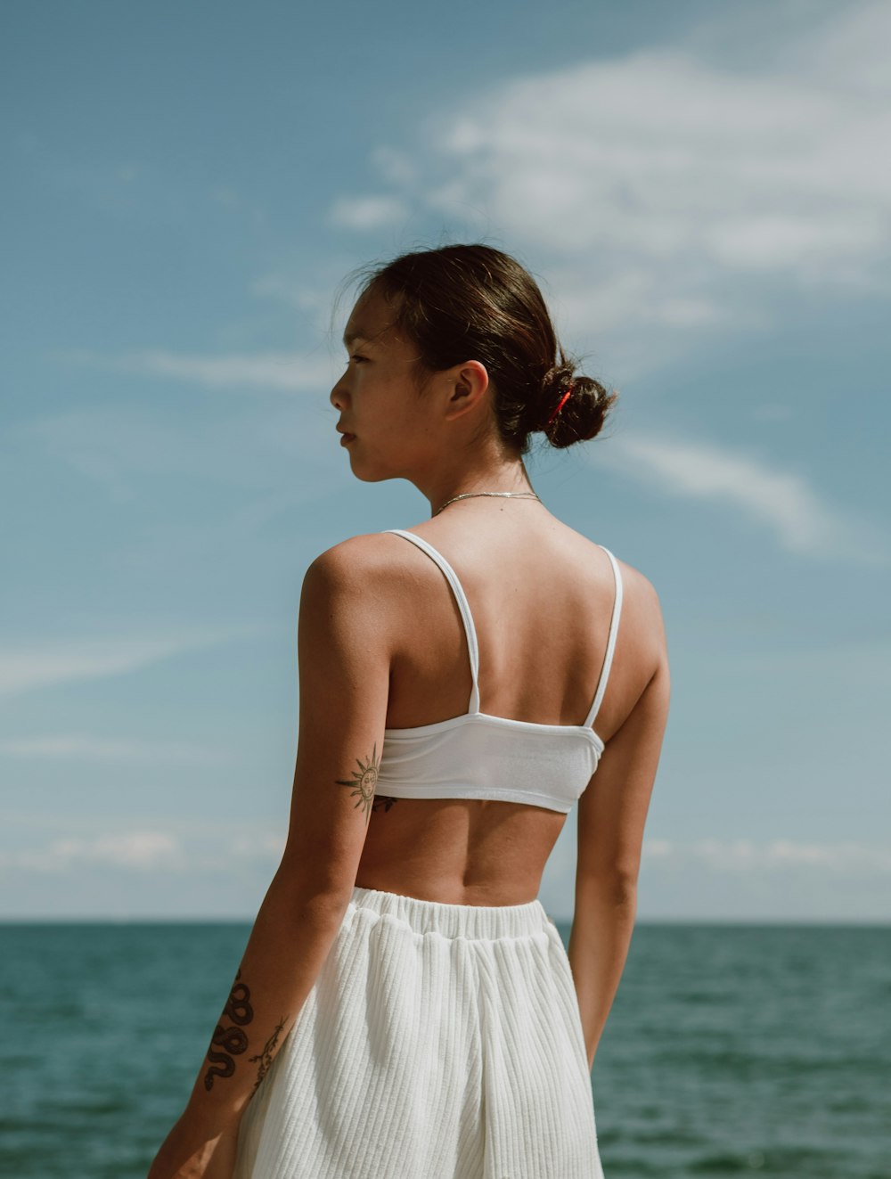 mulher no top branco da alça do espaguete e saia branca em pé na praia durante o dia