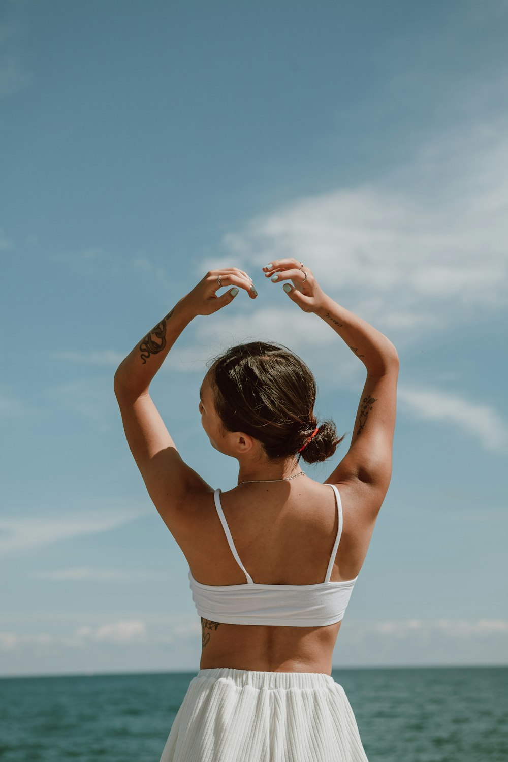 woman in white spaghetti strap top raising her hands