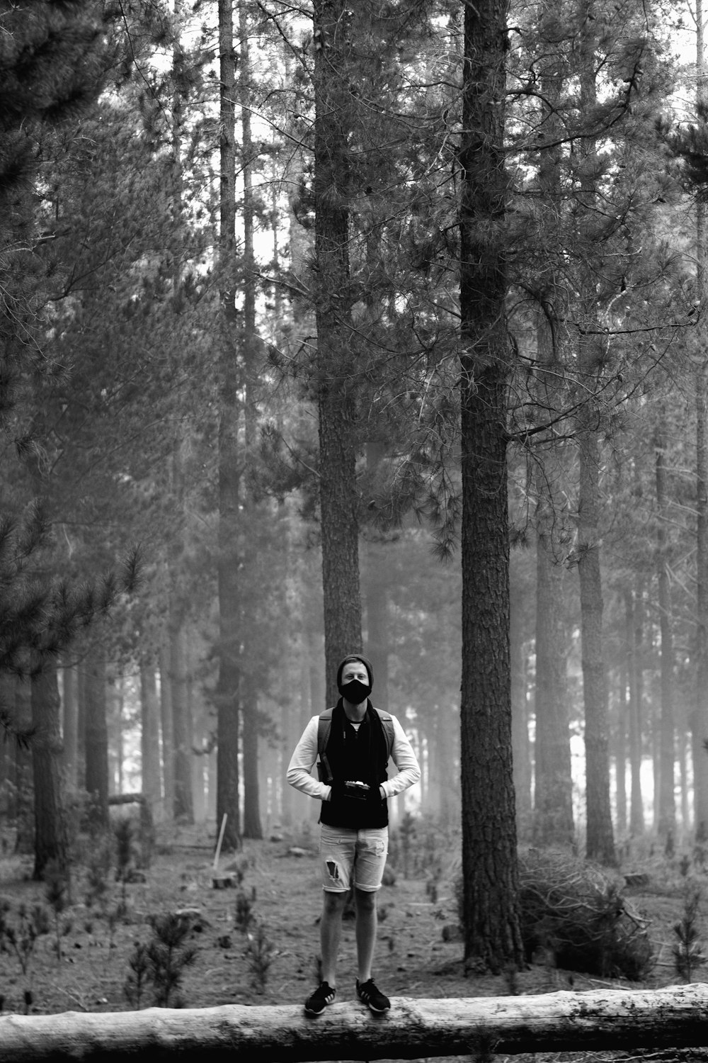 grayscale photo of man in black jacket standing in the middle of forest