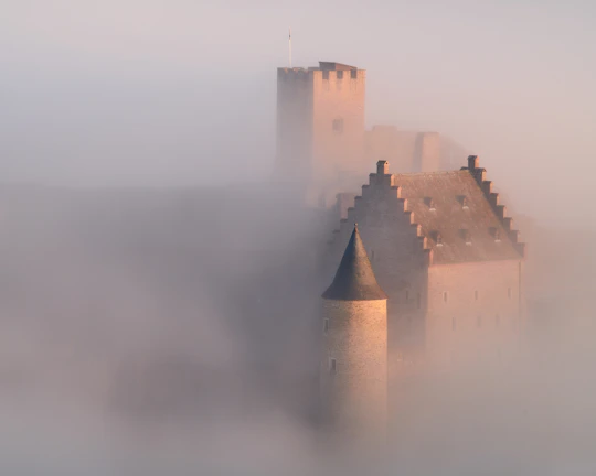 A shadowy ancient castle at dusk with eerie fog surrounding its towers.