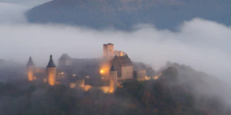 A misty medieval castle courtyard at dawn, with soft light filtering through ancient stone archways.