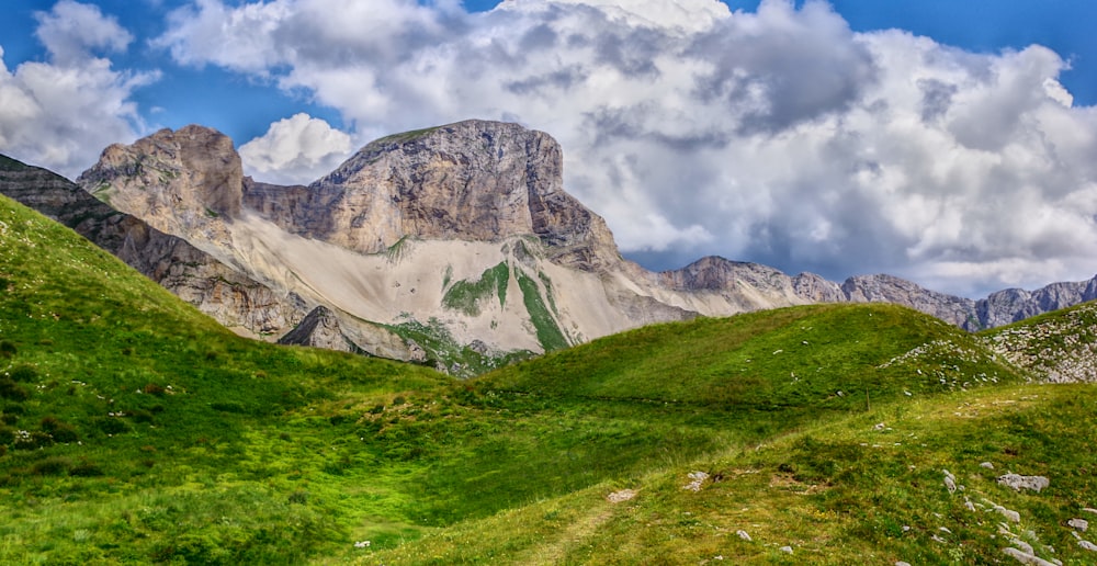 green grass field near mountain under white clouds during daytime