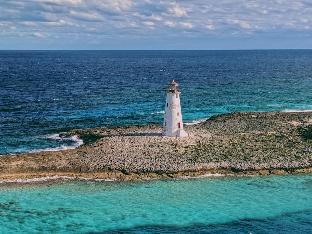 white lighthouse on brown and green grass field near body of water during daytime