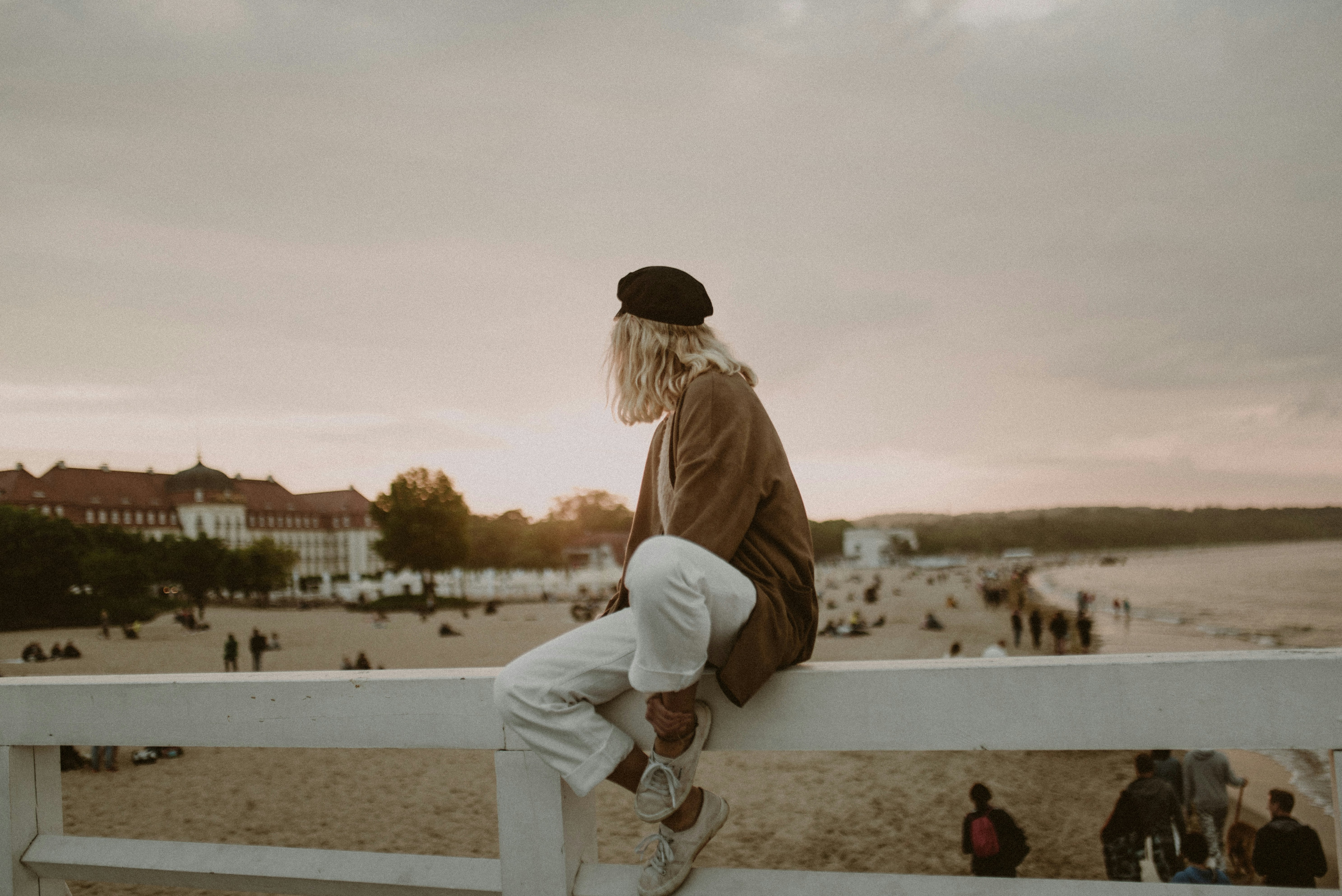woman in brown jacket and black knit cap standing on gray concrete pavement during daytime