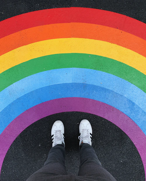 Person in white sneakers standing on a rainbow painted across dark asphalt