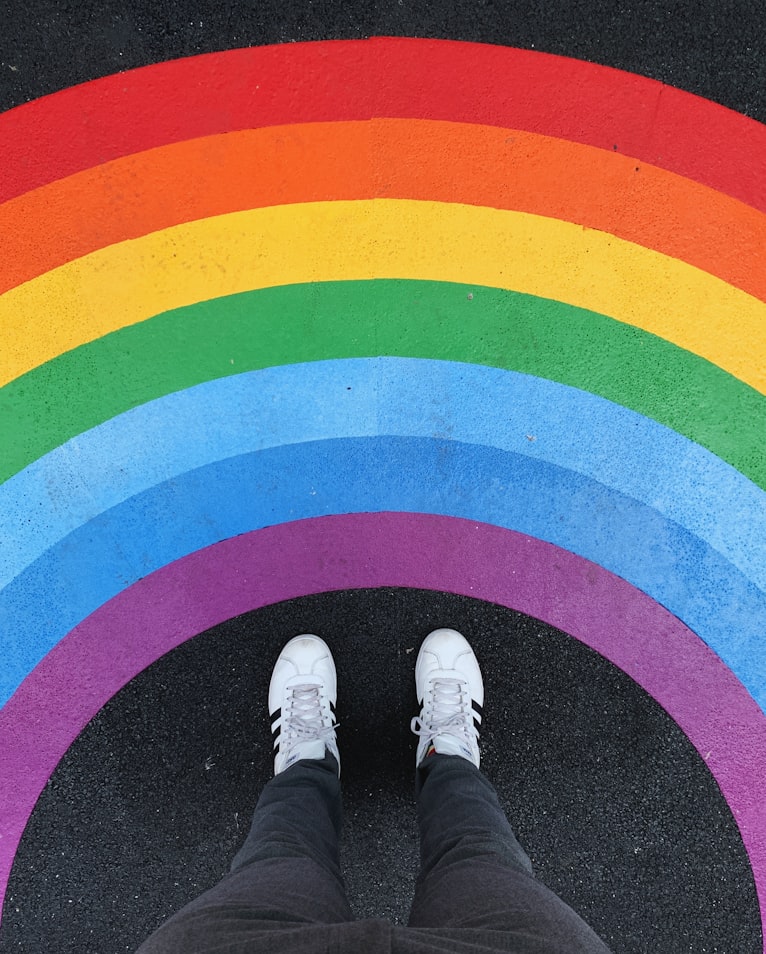 Image is of person looking down at their feet on a black top painted with a huge rainbow