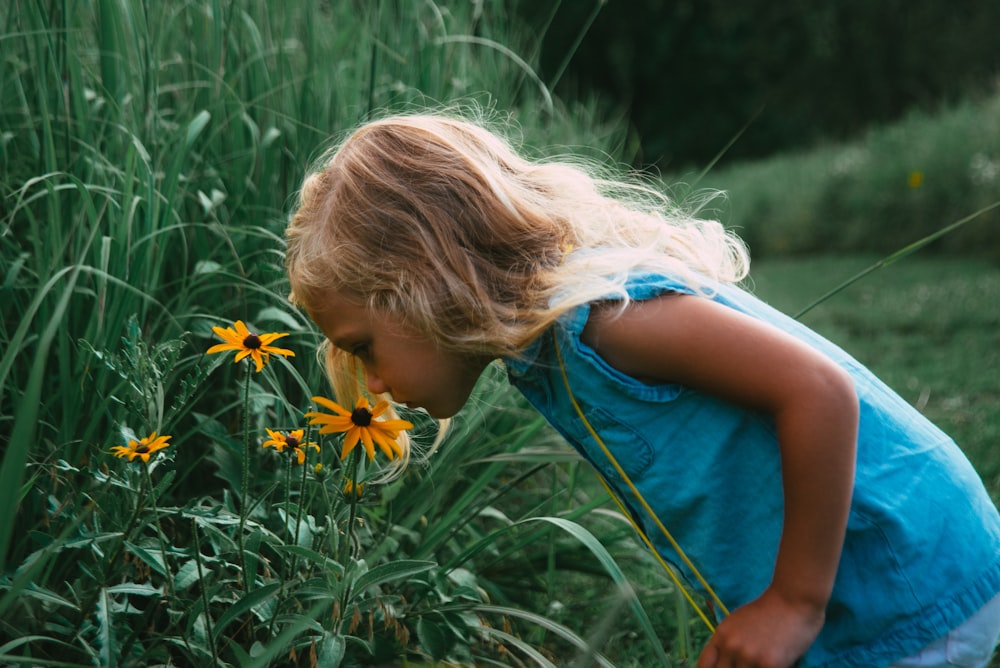 girl in blue sleeveless dress holding yellow flower